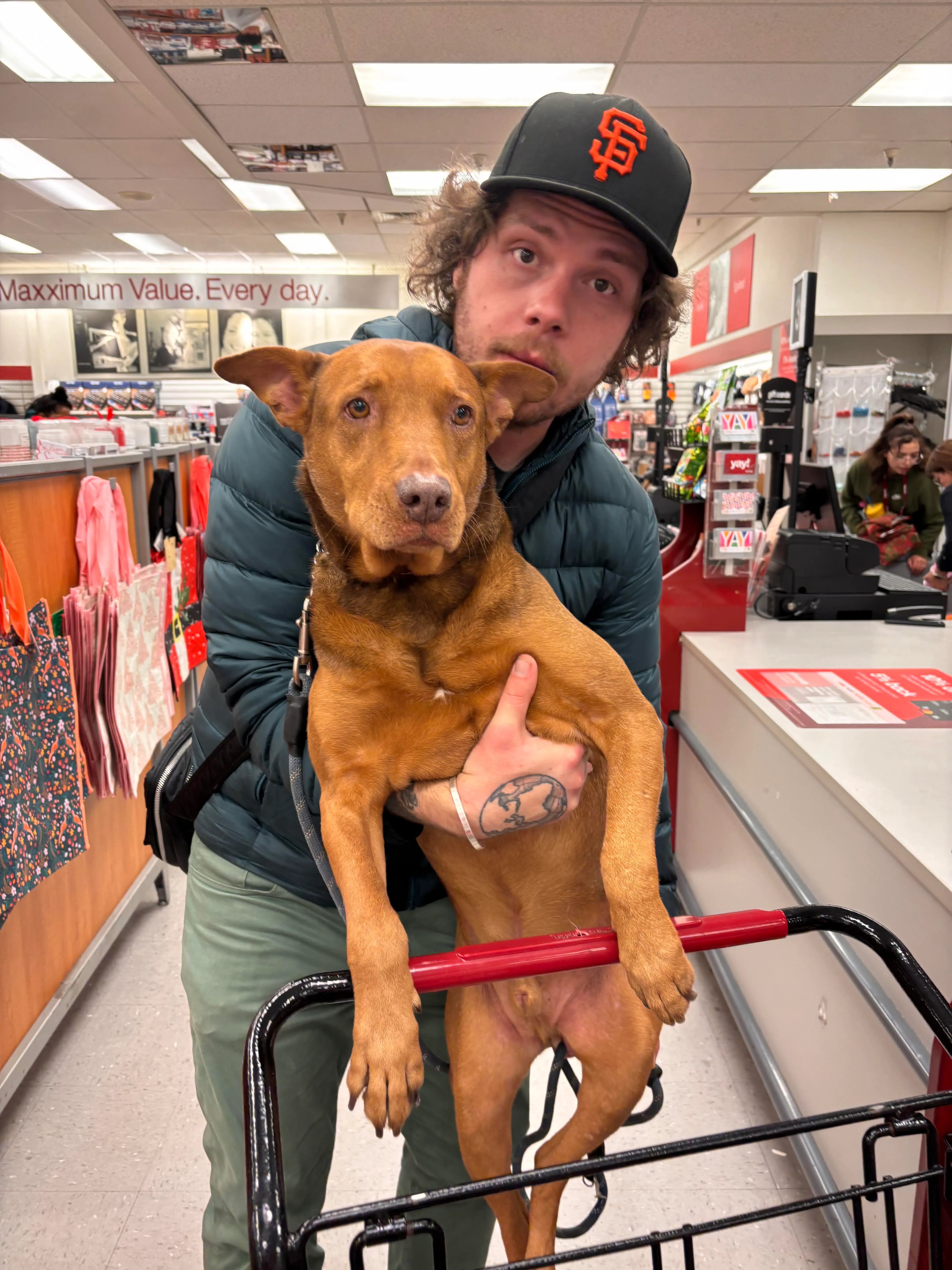 Jacob in an SF Giants cap with a brown dog standing in a shopping cart.